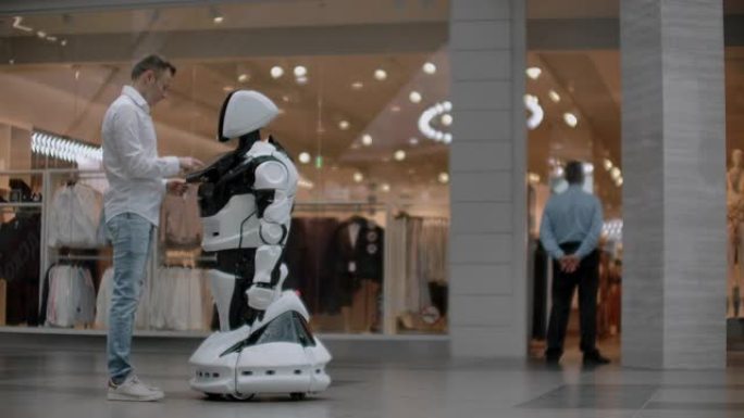 购物中心的那个人与机器人顾问交流。现代商店和机器人卖家。机器人在购物中心帮助一个人