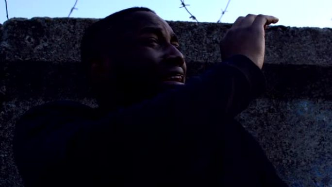 哭泣的黑人难民站在铁丝网后面，政治犯监狱