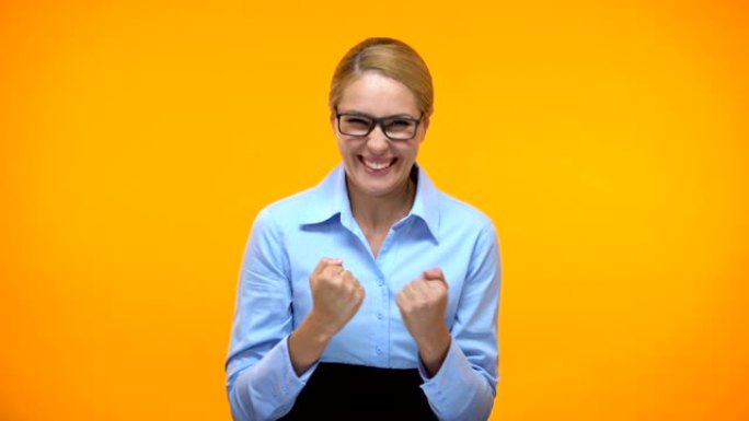 兴奋的女商人表现出成功的姿态橙色背景，职业目标