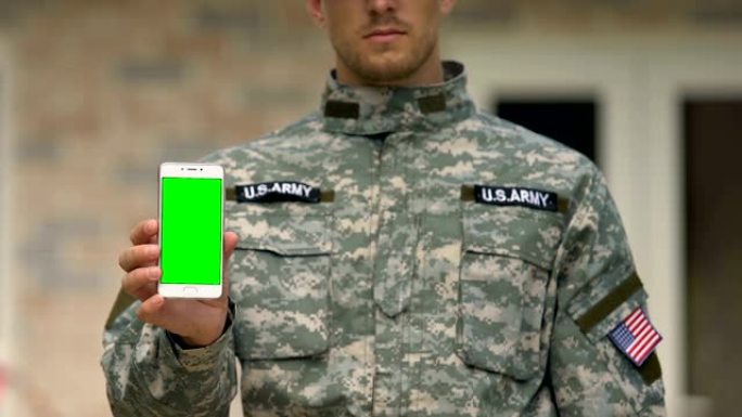 年轻的军人正在展示智能手机的绿屏，陆军支持应用程序，小玩意