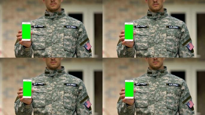 年轻的军人正在展示智能手机的绿屏，陆军支持应用程序，小玩意