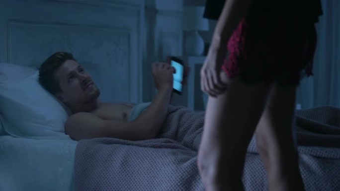 英俊的男性躺在床上聊天电话，诱人的女士在内衣来