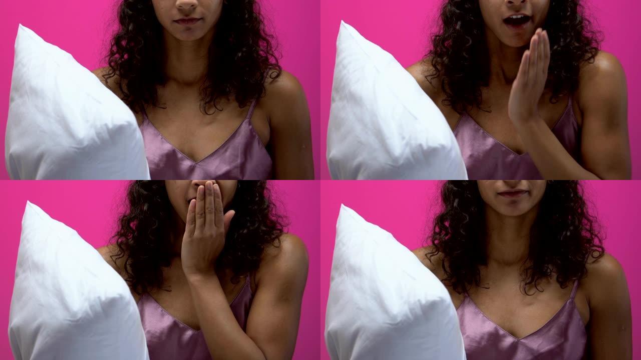穿着睡衣的非裔美国妇女抱着枕头打哈欠，准备睡觉