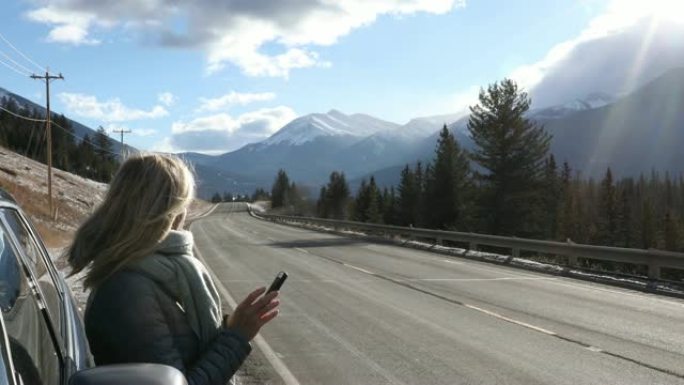 女人在山路上离开车门，检查智能手机