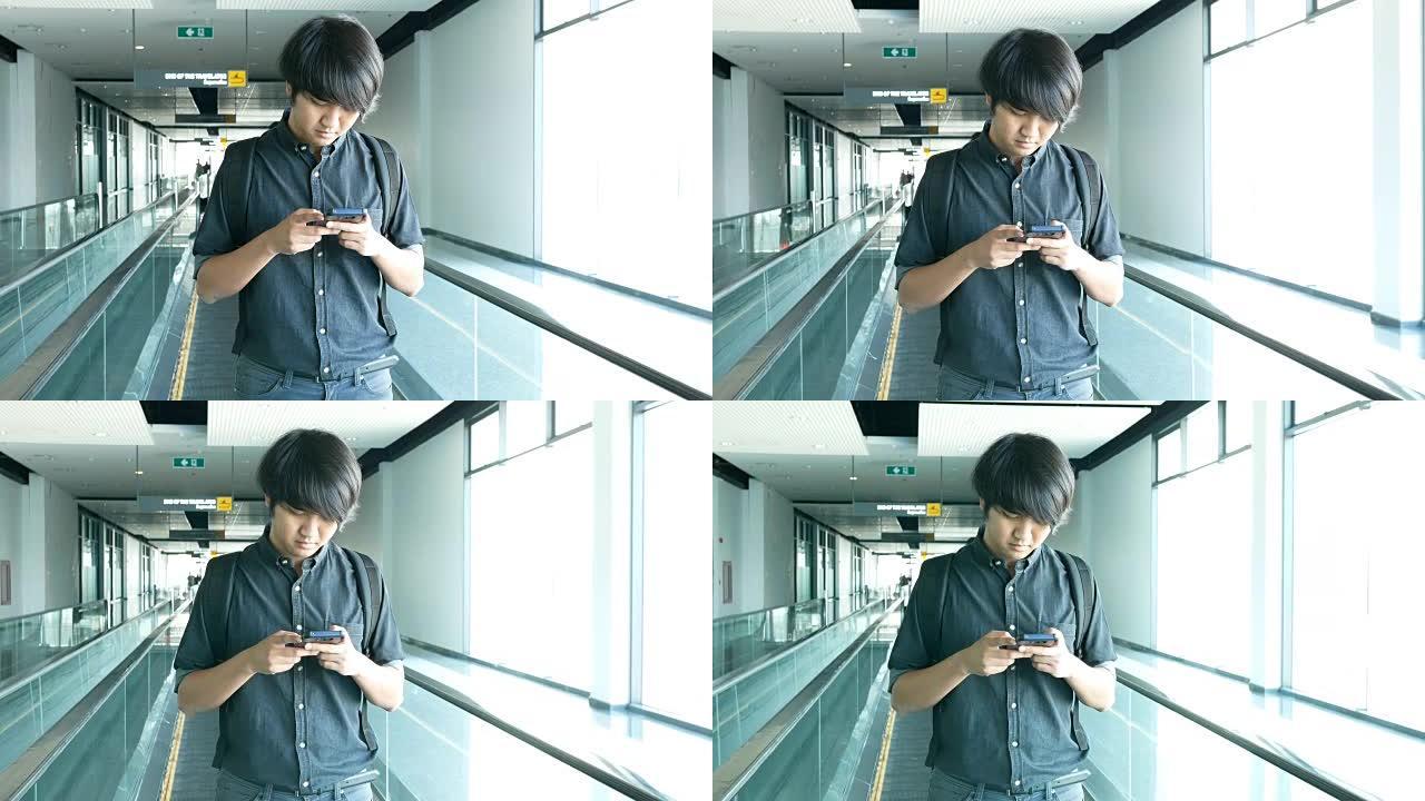 亚洲男子在人行道/自动人行道上使用智能手机。