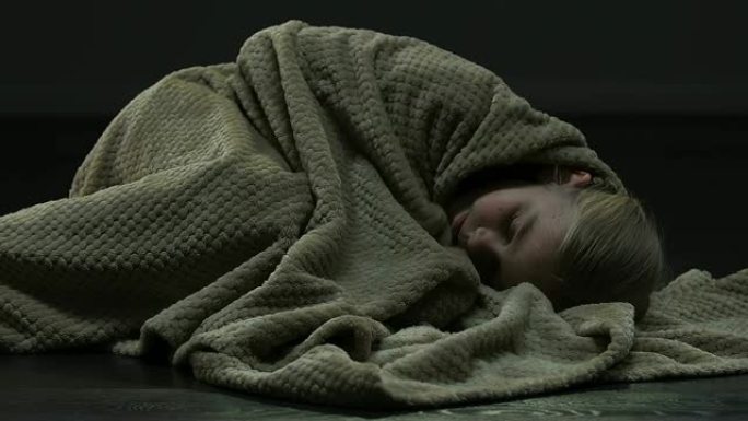 害怕的女孩因恐惧而退缩，躺在地板上，用毯子遮住头
