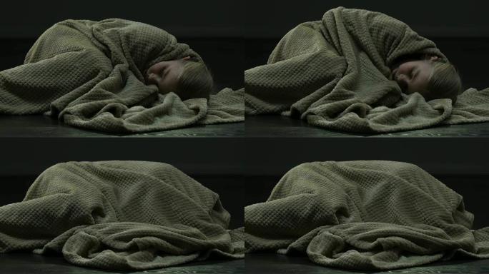 害怕的女孩因恐惧而退缩，躺在地板上，用毯子遮住头