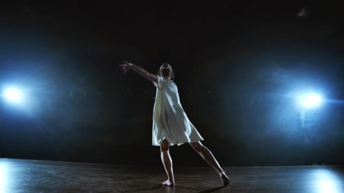 变焦镜头回来，一个穿着白色连衣裙的芭蕾舞女演员跳了起来，开始在聚光灯下在舞台上移动和奔跑，在白色背景