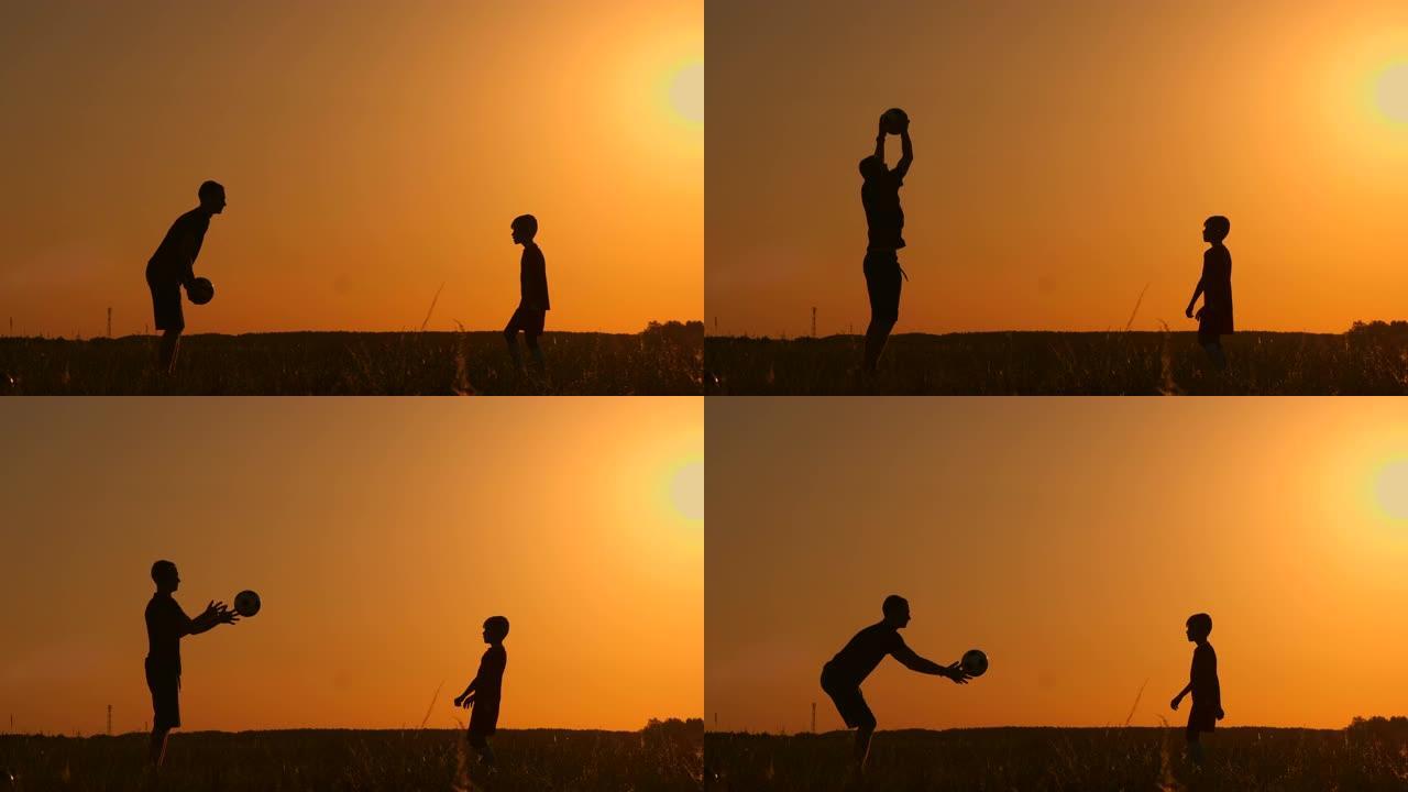 父亲和儿子在日落时在公园踢足球，在灿烂的阳光，慢动作拍摄的背景下剪影