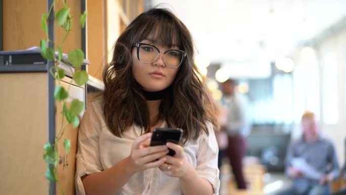 年轻的亚洲女商人在现代办公空间使用手机的肖像