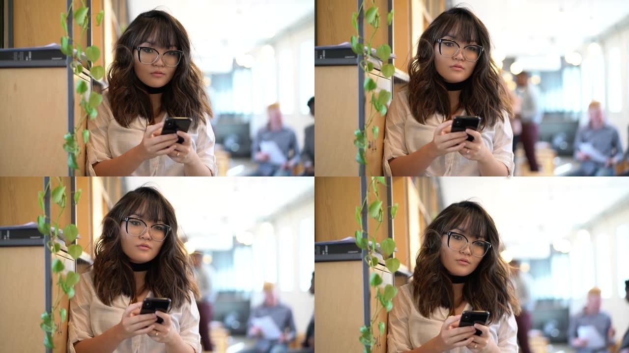 年轻的亚洲女商人在现代办公空间使用手机的肖像