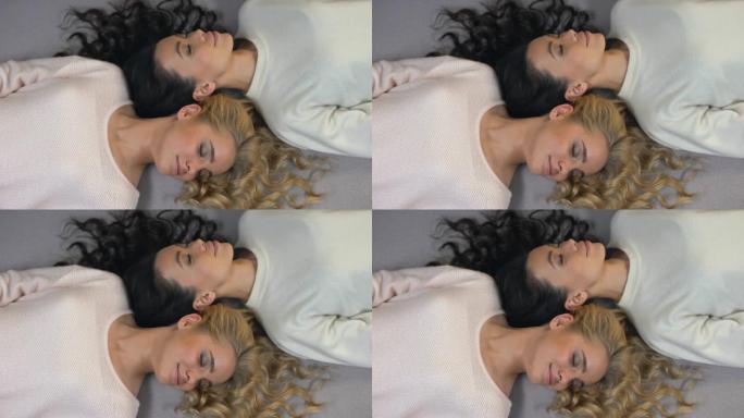 迷人的金发女郎和黑发女人闭上眼睛，躺在地板上，摆姿势拍照