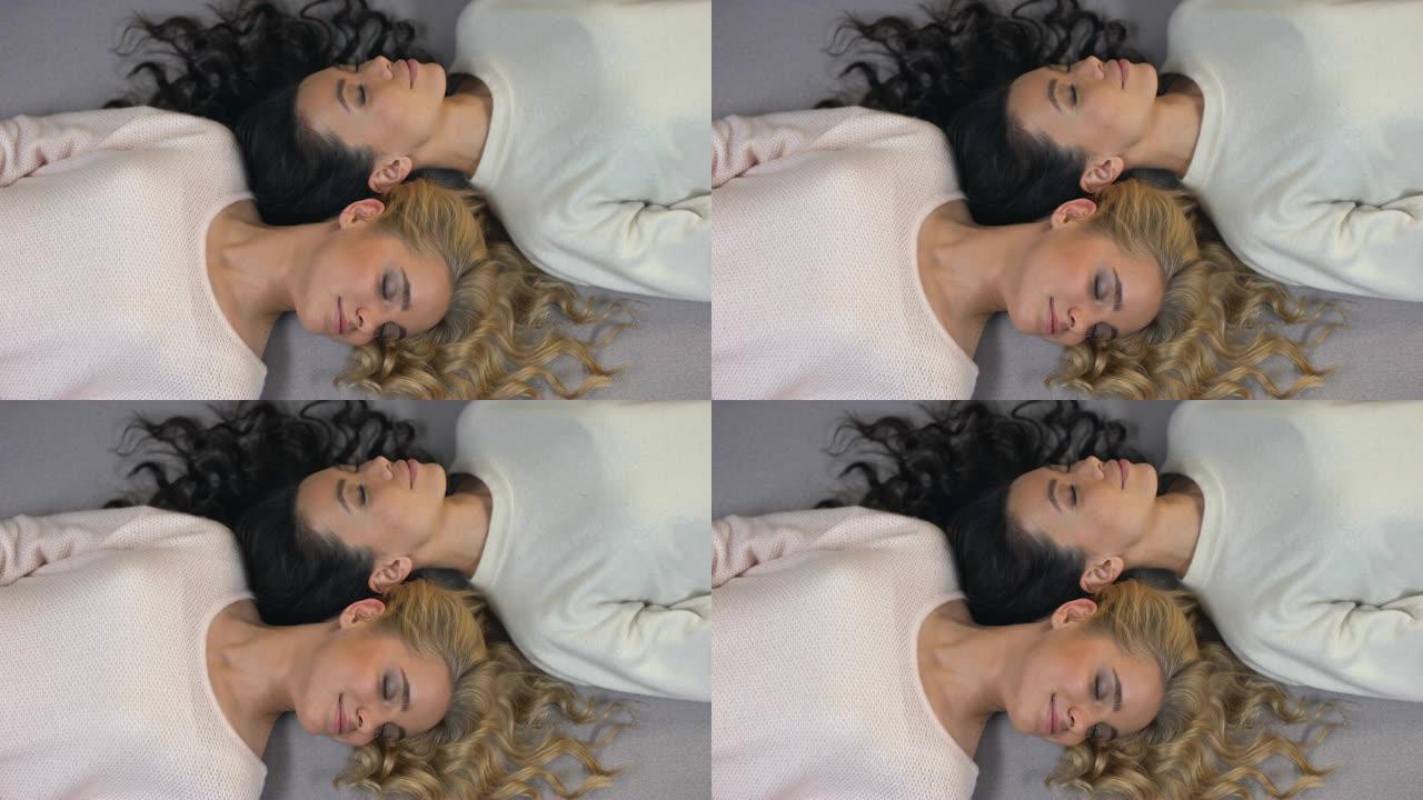 迷人的金发女郎和黑发女人闭上眼睛，躺在地板上，摆姿势拍照