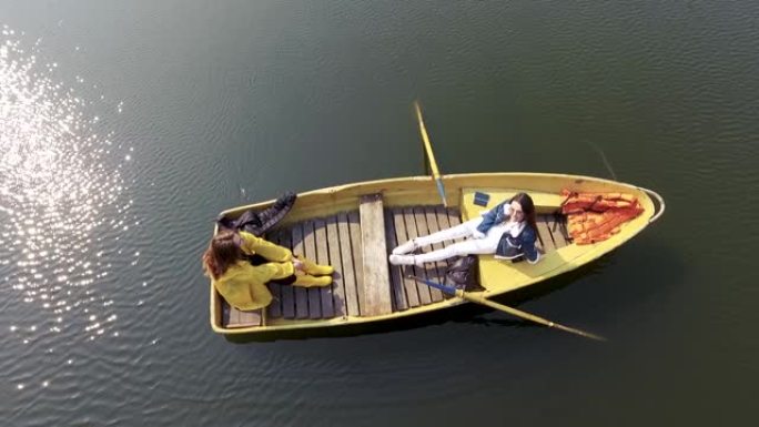 两个年轻漂亮的女孩坐在美丽的反光湖或河中间的小船上。