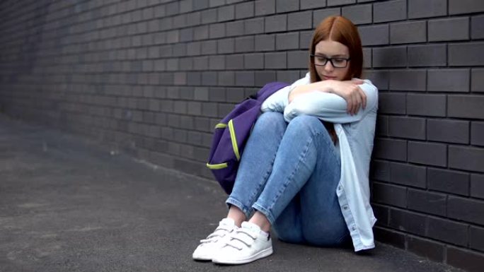 孤独的女学生眼镜坐在高中后院的地板上，问题