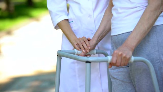 女护士支持残疾老太太，户外步行框架，康复中心