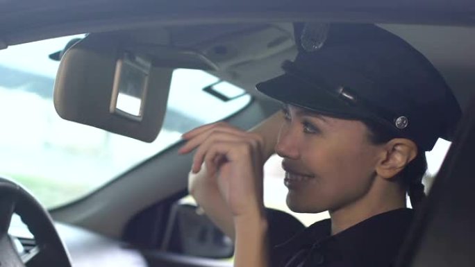 微笑的亚洲女警察调整司机座位上的帽子在巡逻车，职责