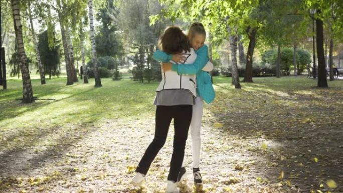母女俩扔树叶拥抱。两个快乐的高加索女人在秋季公园玩得开心