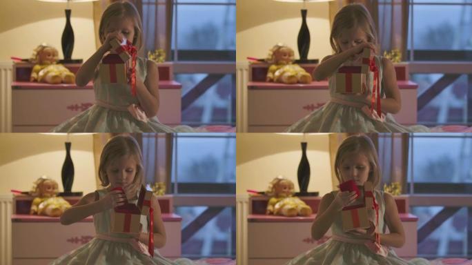 高加索女孩的特写镜头用优雅的蝴蝶结打开棺材，脱下红色的东西。穿着漂亮衣服的小孩坐在家里的房间里。童年
