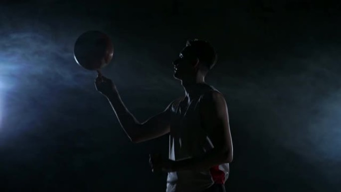 戴兜帽的篮球运动员晚上在空旷的停车场以慢动作旋转球