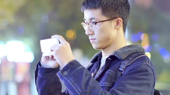 亚洲男子学生晚上在校园里手持手机