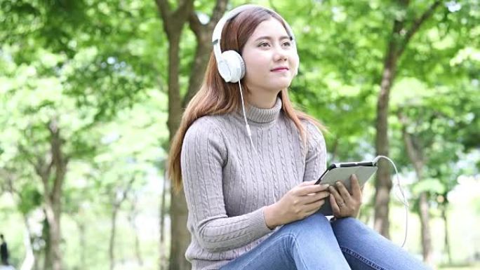 亚洲女性在公园使用平板电脑和耳机放松
