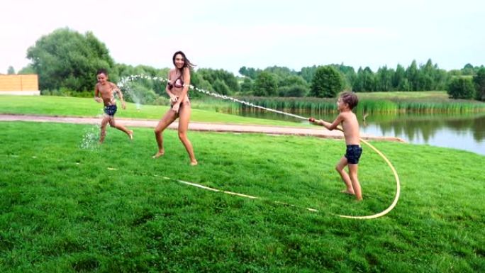 两个男孩和爸爸妈妈在自家后院玩，他们浑身湿透，慢镜头里笑着。幸福的家庭