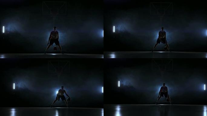 球技运球篮球运动员在黑暗的篮球场上，背光在烟雾中。慢动作街球