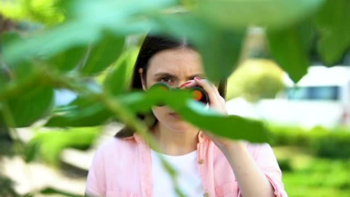 女人用双筒望远镜躲在树后，记者寻找感觉