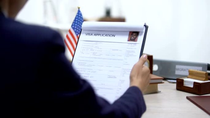 女性移民检查员拒绝签证申请，美国国旗摆在桌面上