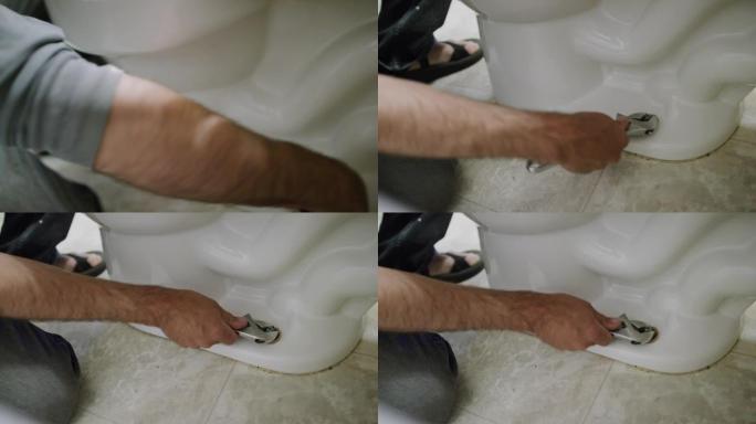 一名高加索修理工在室内家庭浴室中使用可调扳手松开将马桶固定在地板上的螺母