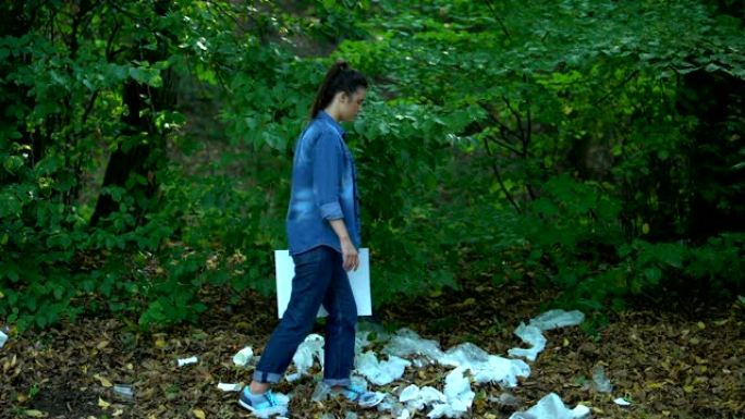 担心的女性手持save planet标志步行森林垃圾填埋场，塑料垃圾
