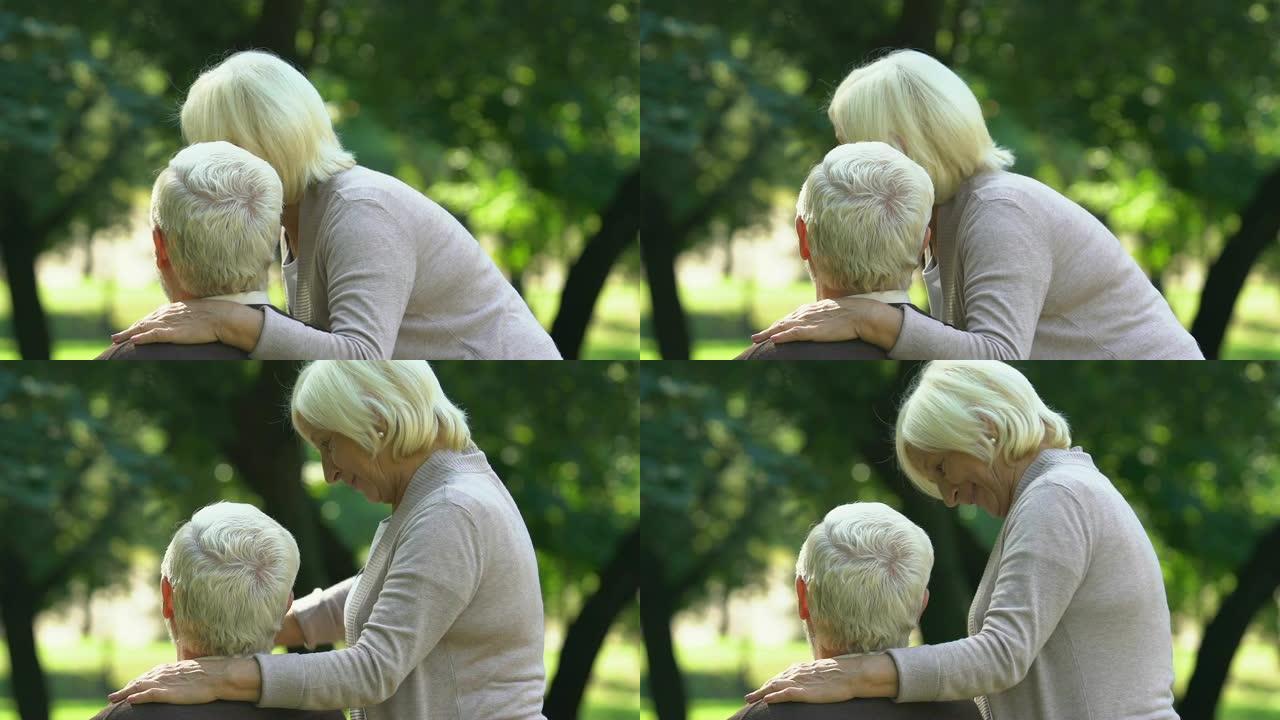 老夫妇亲吻并看着他们的孙子在公园玩耍，后视图