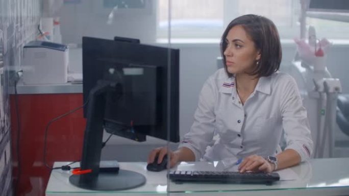 专业女医生在实验室外套上倾斜，在带照明的办公桌上使用透明监视器的未来派计算机打字。适合添加AR元素的