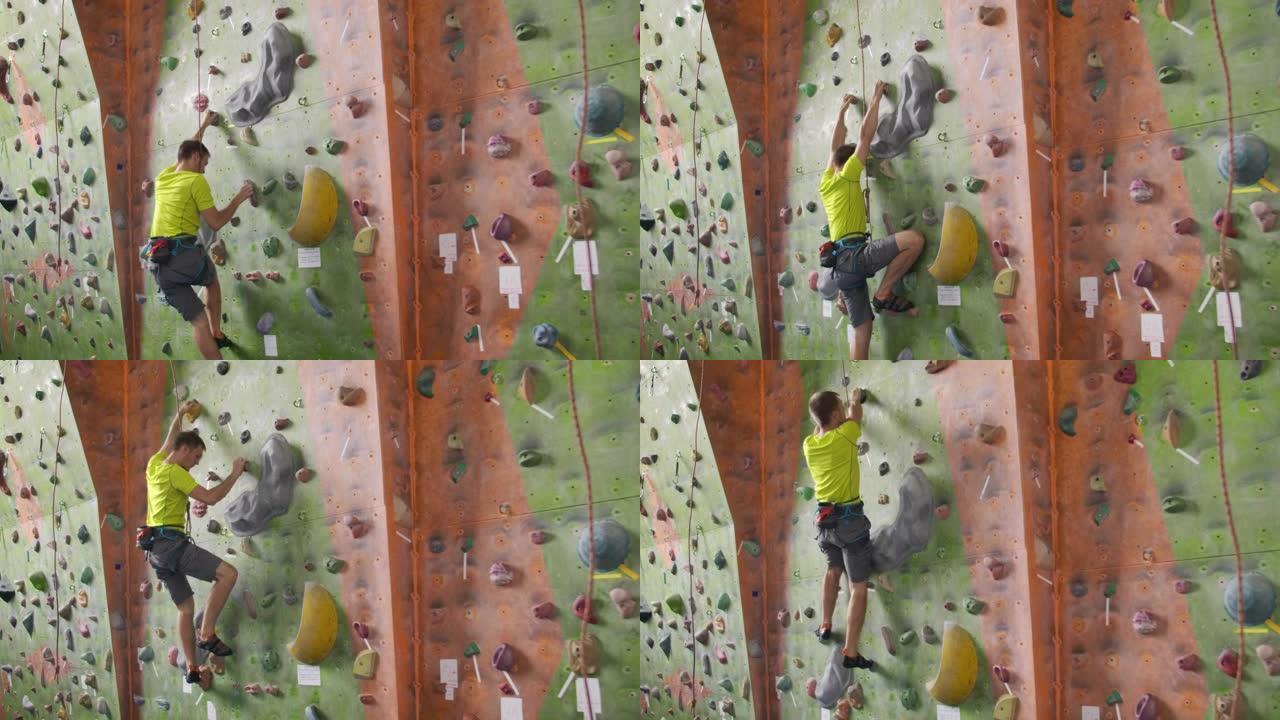 雄性登山者爬上房间里的悬崖墙，伸手抓住。一个专业的集中登山者在墙上移动，相机升起并放下他的动作。繁荣