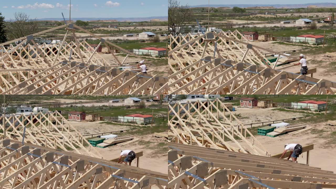 空中无人机拍摄的液压起重机将木制屋顶桁架放下到位，一名高加索男性建筑工人在阳光明媚的日子将房屋固定在