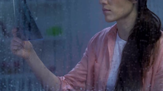 绝望的患病女性在下雨的窗户附近看肺部x射线，患有结核病
