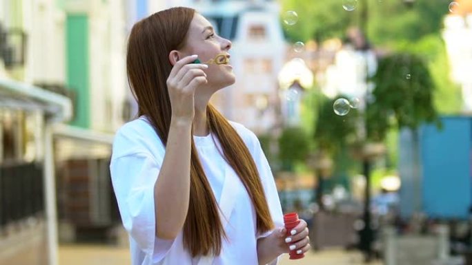 微笑的红发年轻女子在户外吹肥皂泡，在公园玩得开心