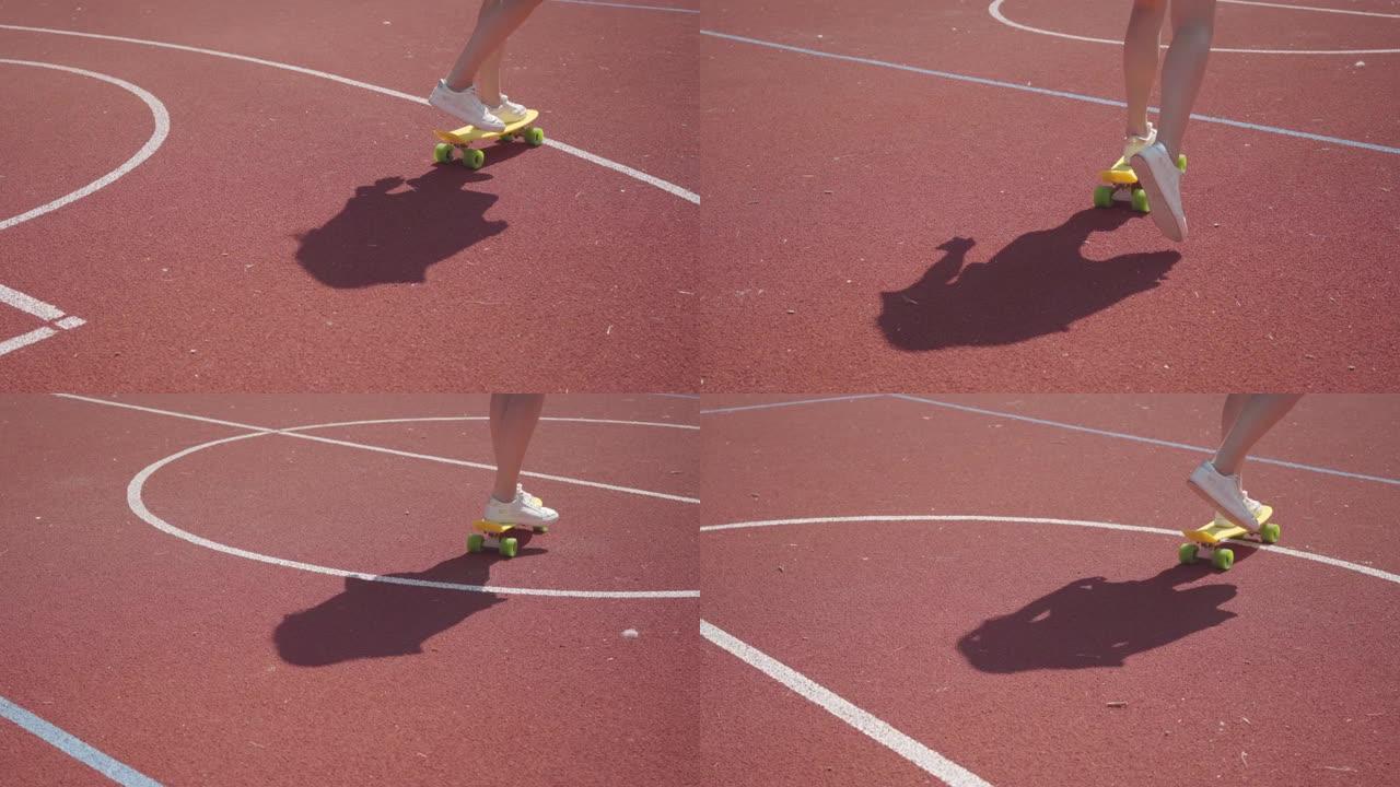 穿着白色运动鞋的女性腿的特写镜头女孩在室外篮球场上骑着黄色滑板。