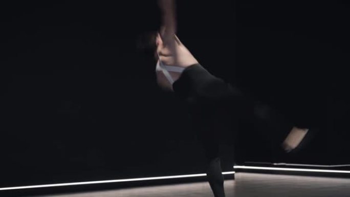专业高加索芭蕾舞演员跳起来，在空中旋转，单膝站立的肖像。自信的年轻人在舞台灯光下跳舞经典舞蹈。慢动作
