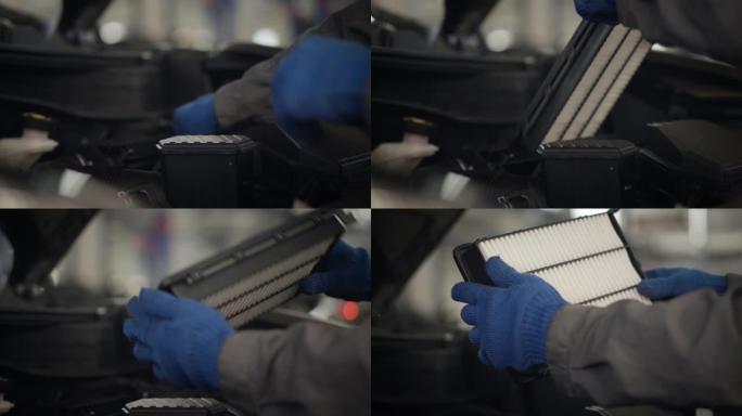 戴着防护手套的男性手的特写镜头取下发动机空气滤清器，并将其放回汽车引擎盖。专业汽车机械师在修理厂检查