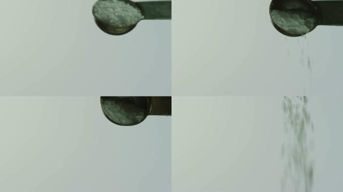 从金属量匙倒出的盐晶体在白色背景上的特写镜头