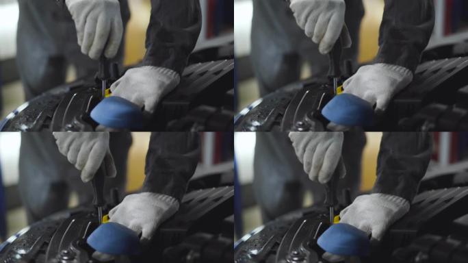 用螺丝刀拧紧敞开式汽车引擎盖上的螺丝，用保护手套中的男性手的特写镜头。修理厂修理或调校汽车的专业工人