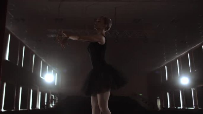 穿着深色连衣裙的优雅女芭蕾舞演员在剧院的黑暗舞台上表演慢动作