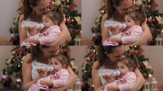 圣诞节那天，母亲在圣诞树下的瓶子里用牛奶喂养她可爱的女婴