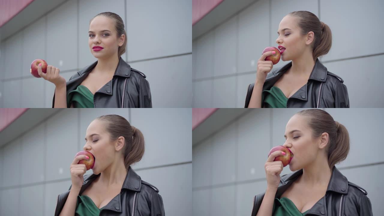 一个可爱的女孩的肖像，在翡翠晚礼服和皮夹克咬一个多汁的苹果。