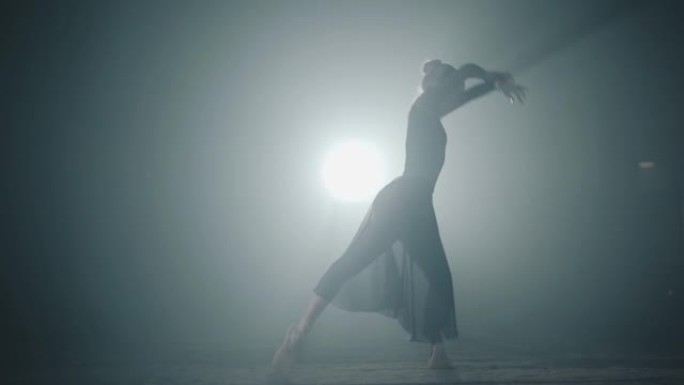 优雅勤奋的芭蕾舞演员在聚光灯下的工作室里穿着黑色连衣裙跳舞