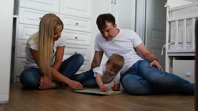 一个穿着白色t恤和蓝色牛仔裤的三口之家坐在卧室的地板上，与男孩一起玩智力游戏。慢镜头拍摄幸福家庭