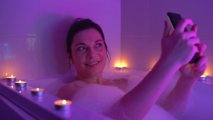 快乐的女人在泡沫水中摆姿势自拍，享受浴室放松