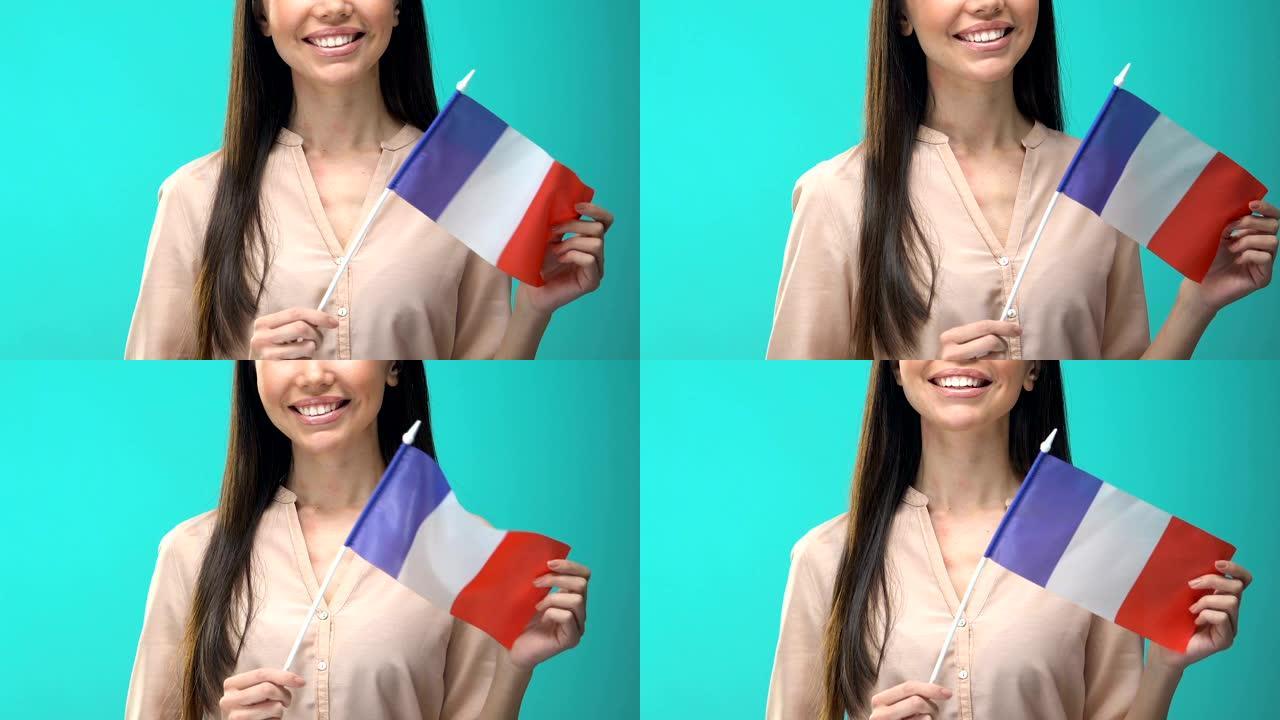 微笑的女人在蓝色背景上举着法国国旗，学生交流计划